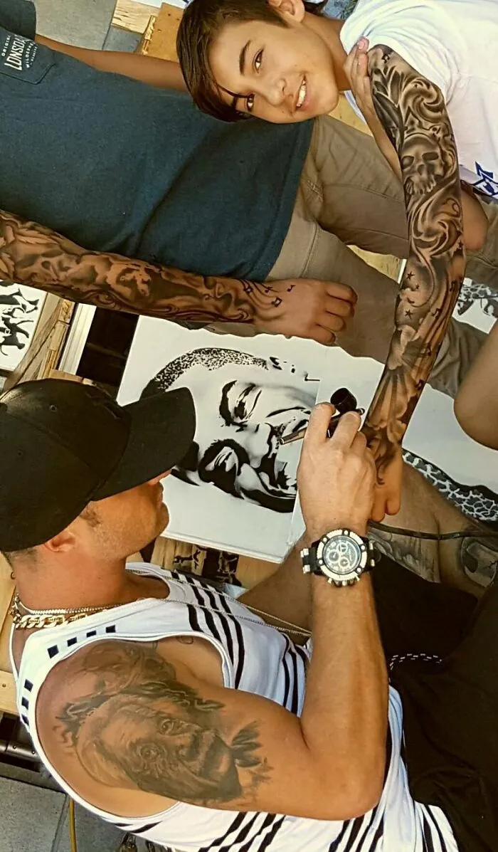 "Artist giving a child a spray-on tattoo, creating a vibrant design on the boy's arm."