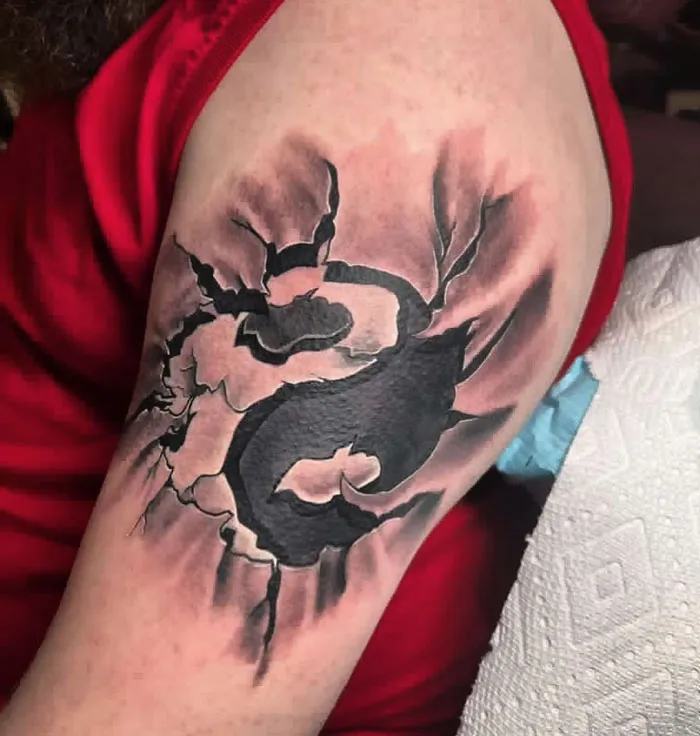 Yin Yang tattoo on upper arm with cracked effect, symbolizing duality.