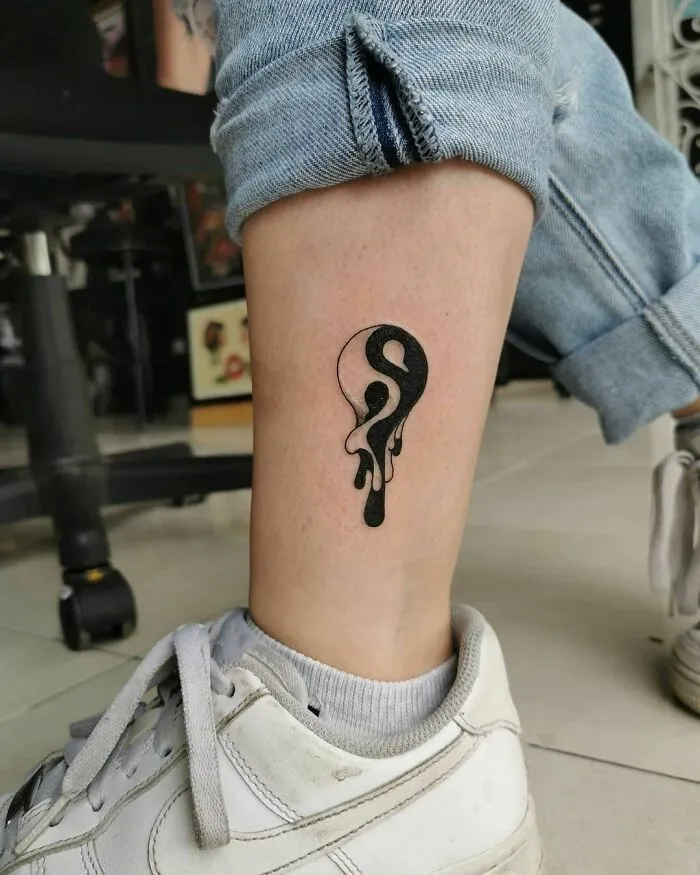 Yin Yang tattoo with artistic drip design on a person's ankle, showcasing the duality of life.