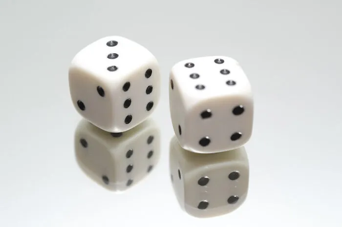 Pair of white dice reflecting on a mirror surface, illustrating unique and interesting useless facts to impress friends.