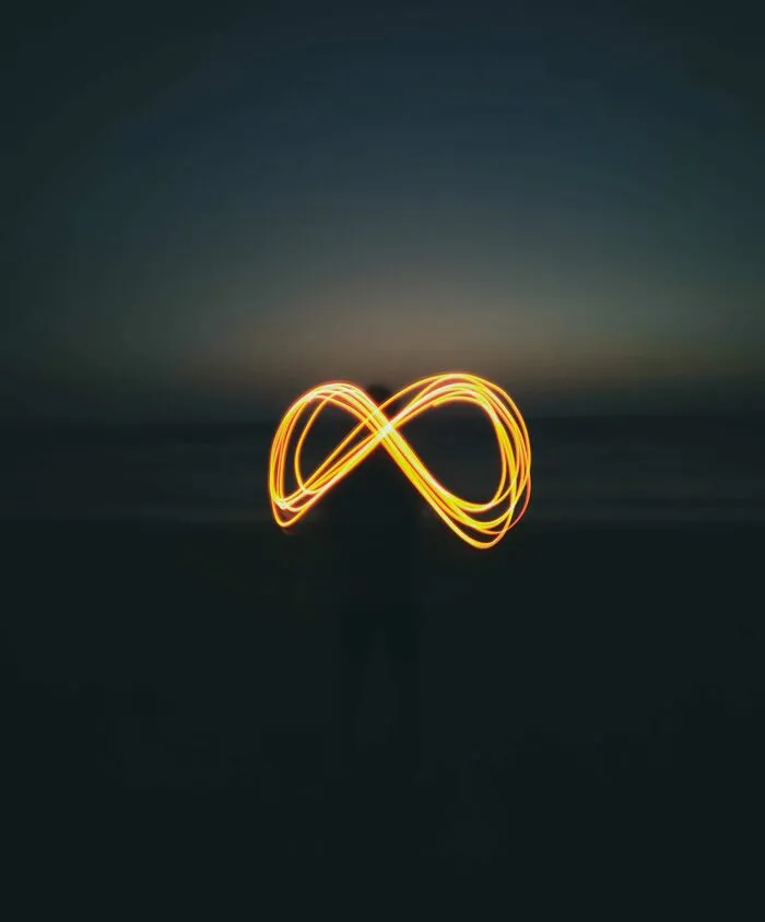 Person creating an infinity symbol with sparkling light at night, illustrating quirky useless facts to impress friends.