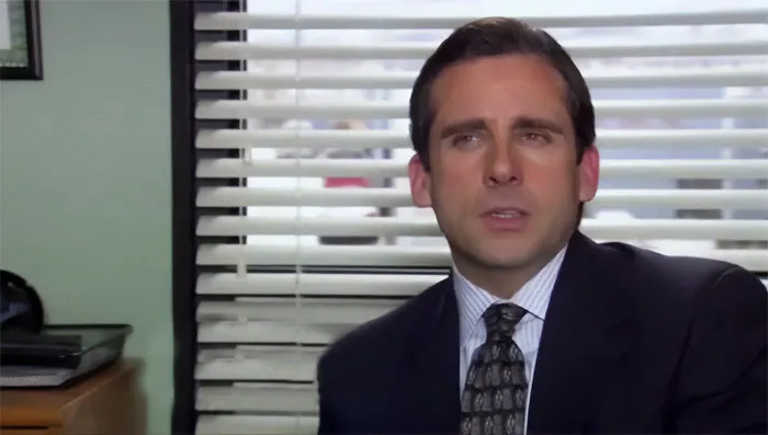 Michael Scott in office setting, dressed in suit and tie, speaking thoughtfully as the best boss ever in quotes collection.