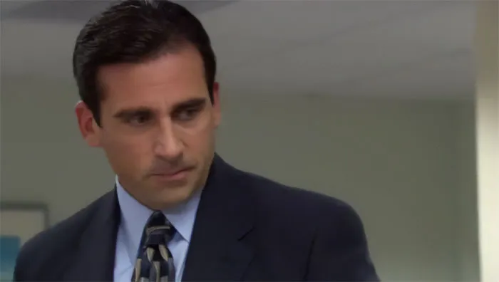 Michael Scott looking down in an office setting, capturing a thoughtful moment with best boss ever vibes.