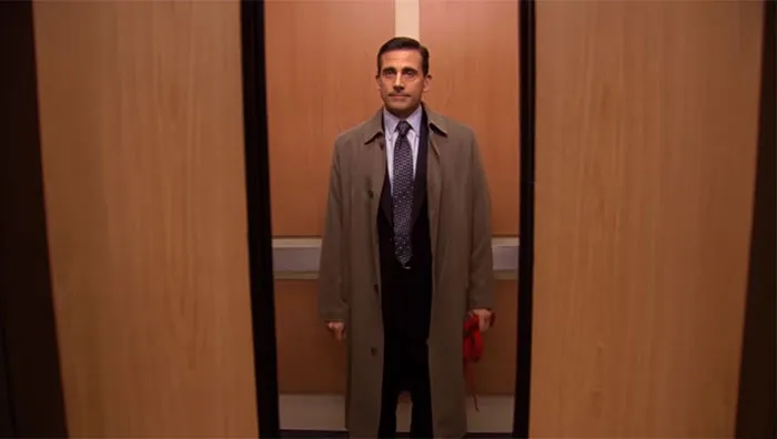 Michael Scott, the best boss ever, standing patiently in an elevator with a coat and tie, waiting for the door to close.