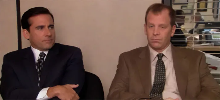 Michael Scott in a suit talking to Toby in an office setting, showcasing memorable Michael Scott quotes as best boss ever.