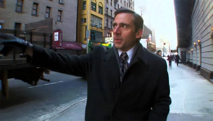 Michael Scott walking down a city street wearing a black coat and suit, embodying the best boss ever vibe.