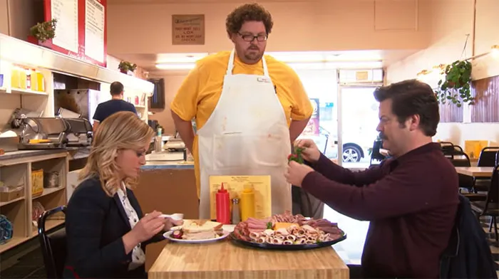 Ron Swanson removing salads from a large meat platter at a diner, highlighting his love for meat in life quotes.