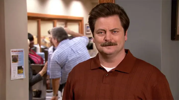 Ron Swanson smiling at the camera wearing a brown shirt, capturing a moment for Ron Swanson quotes on life.