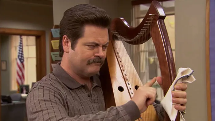 Ron Swanson playing a harp indoors with a focused expression, illustrating a rare moment from Ron Swanson quotes.