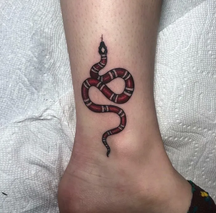 Red and black snake tattoo on ankle, showcasing intricate snake tattoo design.