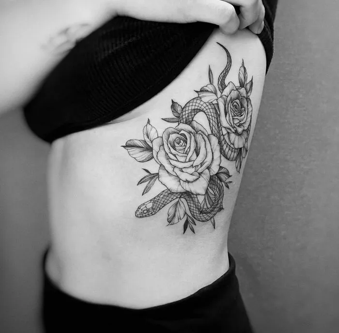Snake tattoo design featuring two roses, inked on a person's side.
