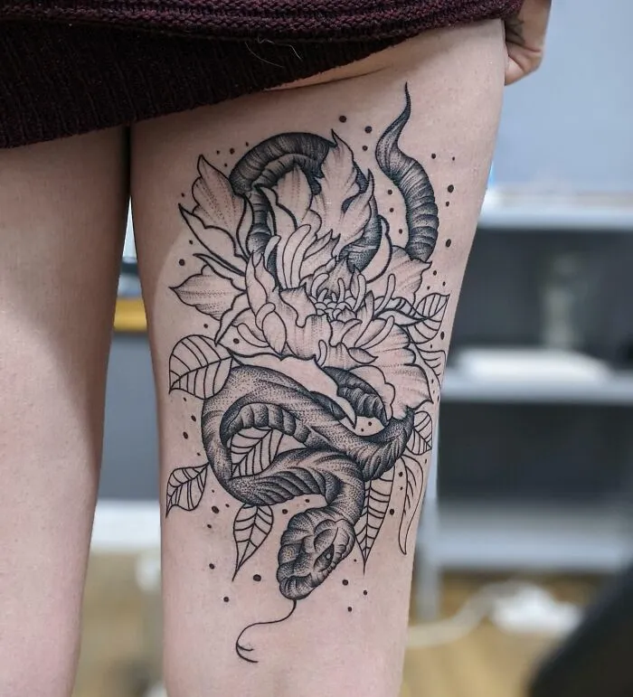 Snake tattoo on thigh entwined with floral design, showcasing intricate linework and shading.