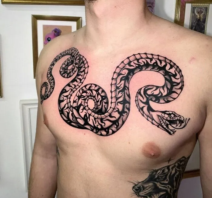 Chest snake tattoo with intricate patterns and details on a person standing indoors.