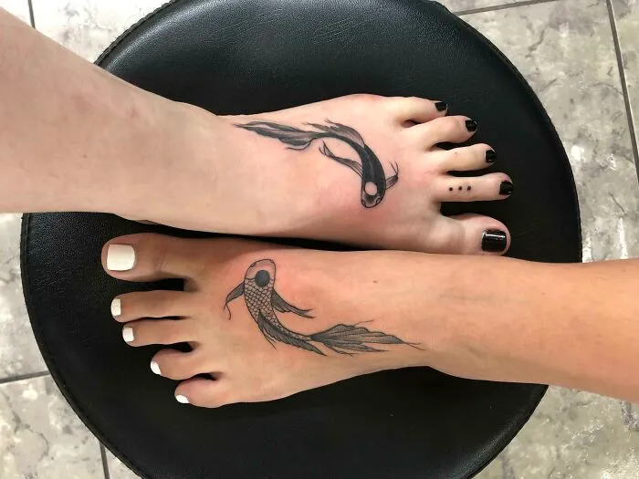 Two feet with matching family bond tattoos of koi fish on a black chair, symbolizing connection and unity.