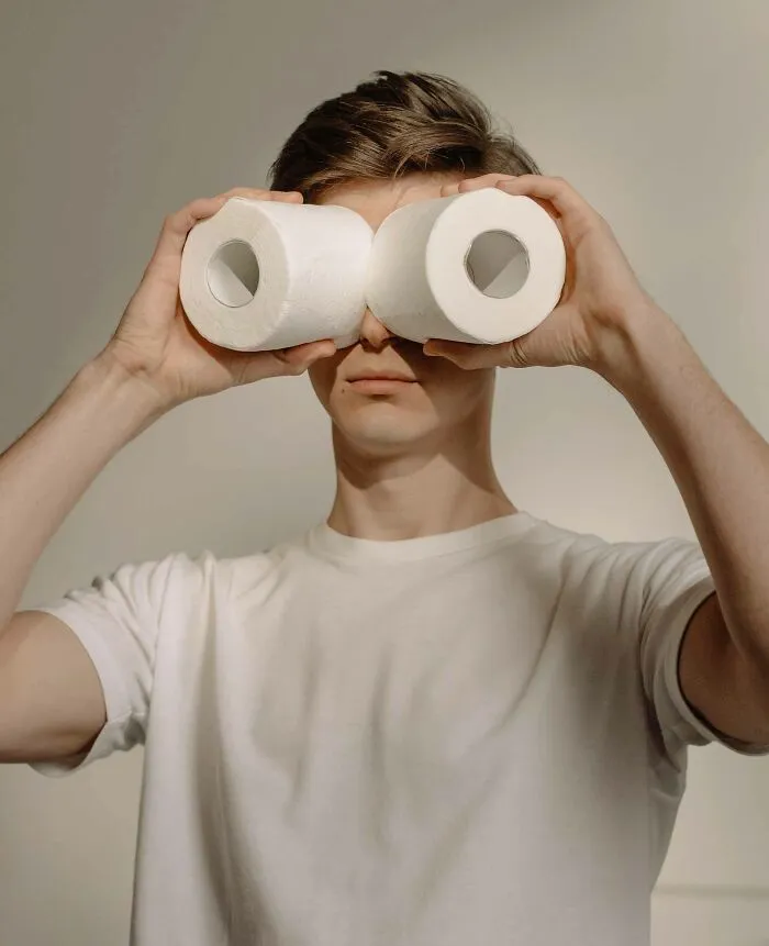 A man in a white t-shirt holding two white tissue rolls over his eyes showing unusual useless facts humor concept.