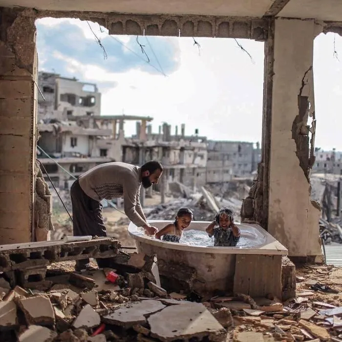 Padre bañando a su hija y a su sobrina en su casa bombardeada en Gaza, 2015, por @emadsnassar