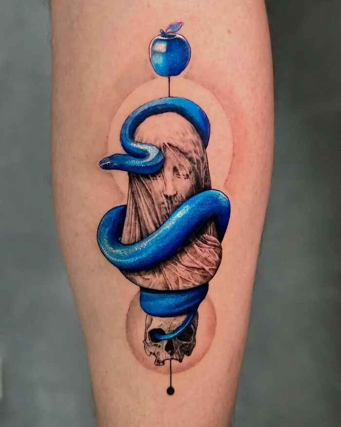 Blue snake tattoo wrapped around a statue with an apple and skull, showcasing intricate design.
