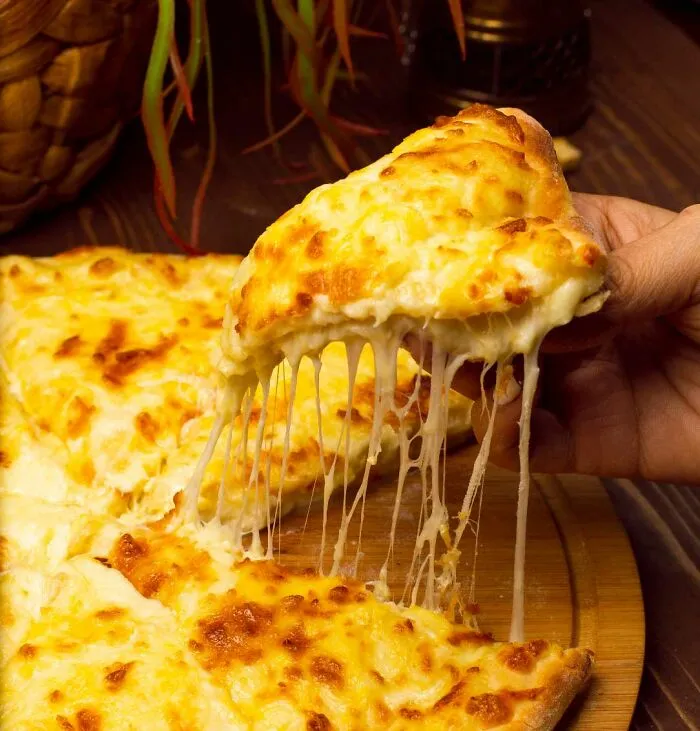Slice of cheesy pizza being lifted with melted cheese stretching, perfect for sharing useless facts to impress friends.
