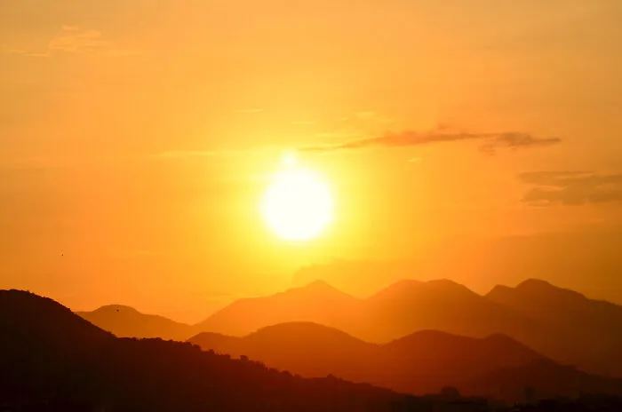 Bright sun shining above mountain silhouettes during a golden sunset, perfect for sharing useless facts to impress friends.