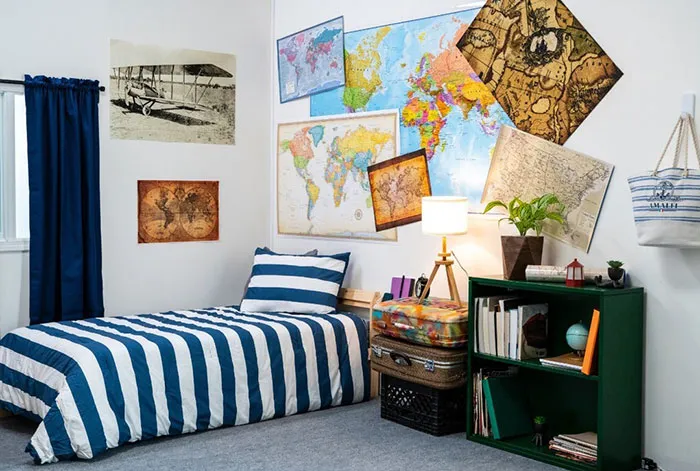 Bedroom wall decor ideas featuring various world maps arranged above a bed with striped bedding and a cozy lamp.