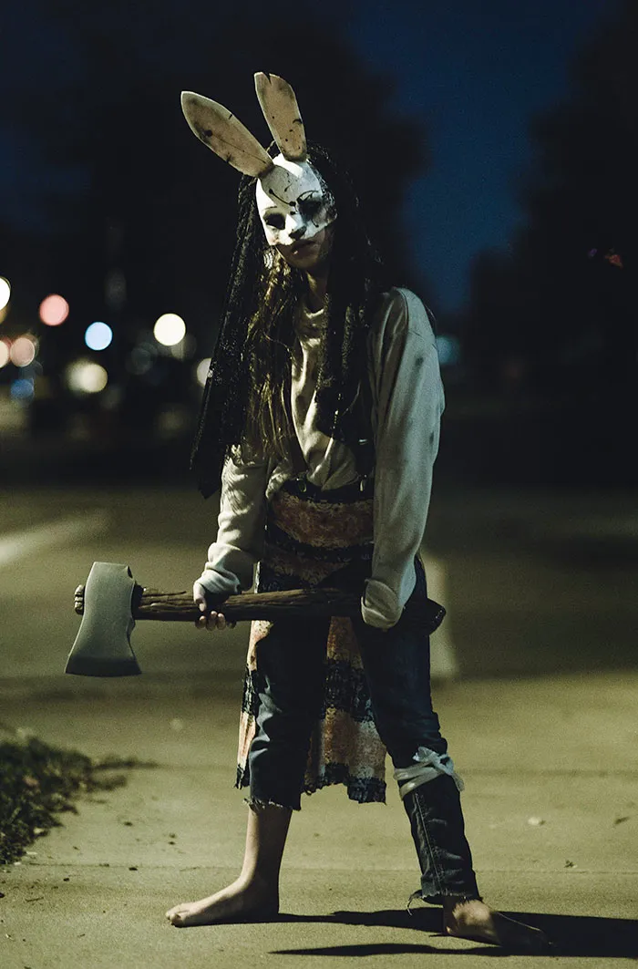 Person wearing a clever Halloween costume with a creepy bunny mask and holding an axe outdoors at night.