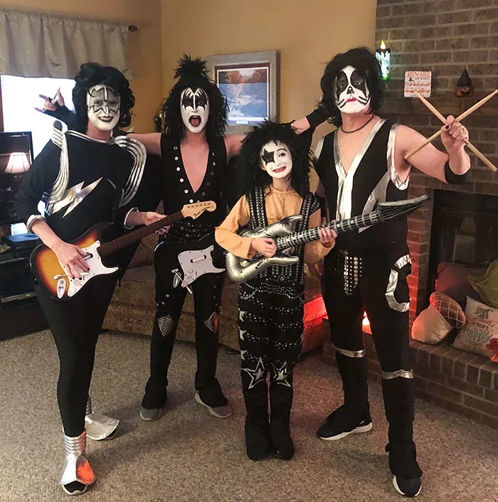Group dressed in clever Halloween costumes as rock band members with painted faces and musical instruments indoors.