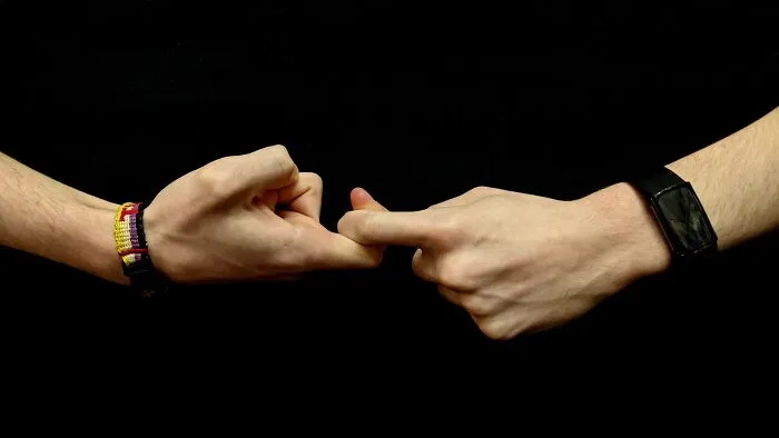 Two hands engaging in a finger lock gesture, wearing colorful wristbands, reflecting shower thoughts questions.