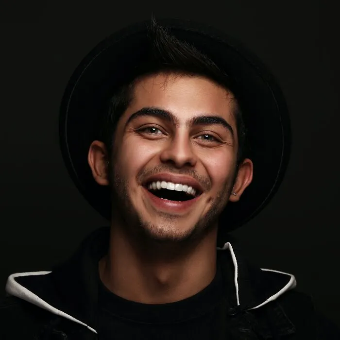 Smiling man in a black hat, captured in a moment of joy, illustrative of engaging shower thoughts questions.