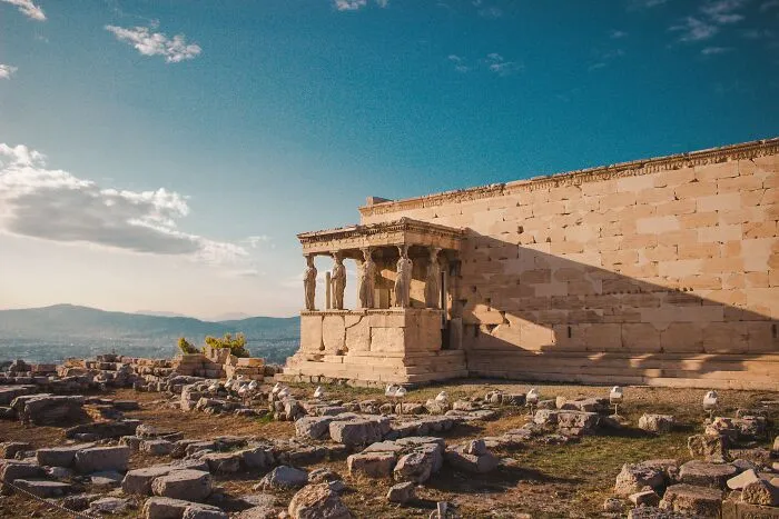 Ancient Greek ruins with statues under a clear blue sky, evoking reflection reminiscent of shower thoughts.