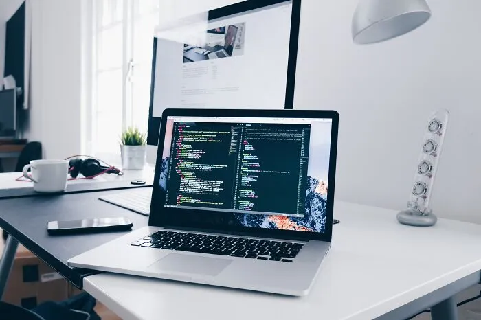 Laptop on desk displaying code, with another monitor in the background, highlighting a tech workspace and shower thoughts questions.