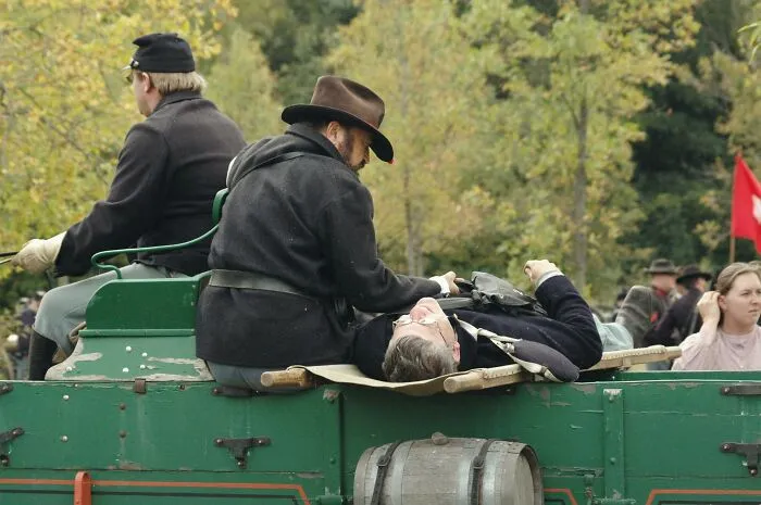 People dressed in historical clothing ride a wagon in a reenactment event.