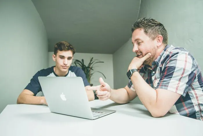 Two people engaged in a discussion at a table, focusing on shower thoughts questions over a laptop.