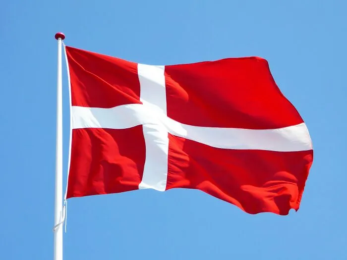 Danish flag waving against a clear blue sky, evoking cultural shower thoughts.
