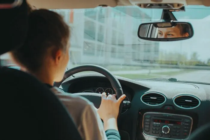 Person driving a car, glancing in the rearview mirror, possibly pondering shower thoughts questions.