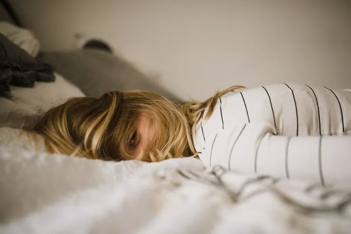 Person lying on a bed, partially hidden by their hair, in a reflective mood resembling shower thoughts.