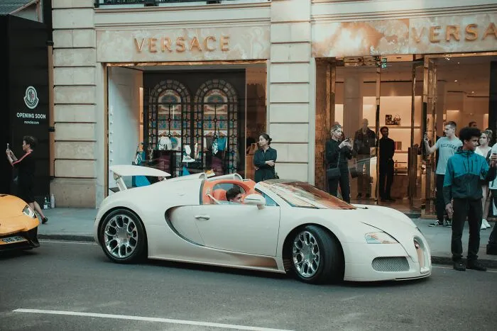 Luxury car parked outside Versace store, drawing attention from passersby, encapsulating a unique shower thought moment.