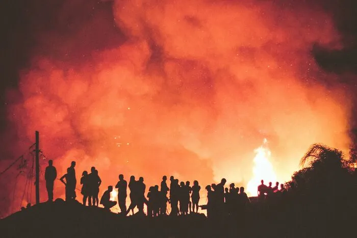 Silhouettes of people against a large fire, prompting deep shower thoughts questions in the vivid scene.