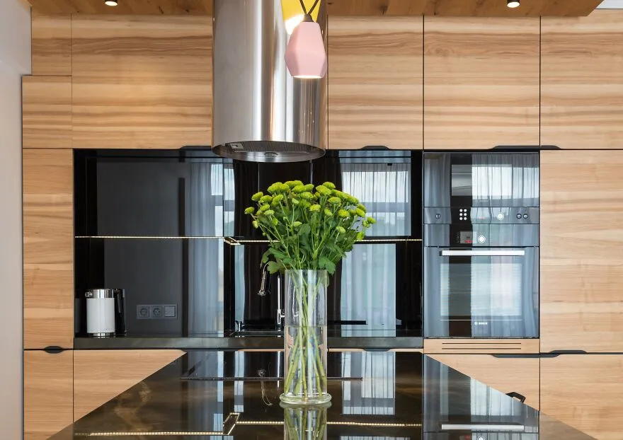 Wooden modern kitchen cabinets with built-in appliances and a stainless steel range hood in a stylish kitchen design.