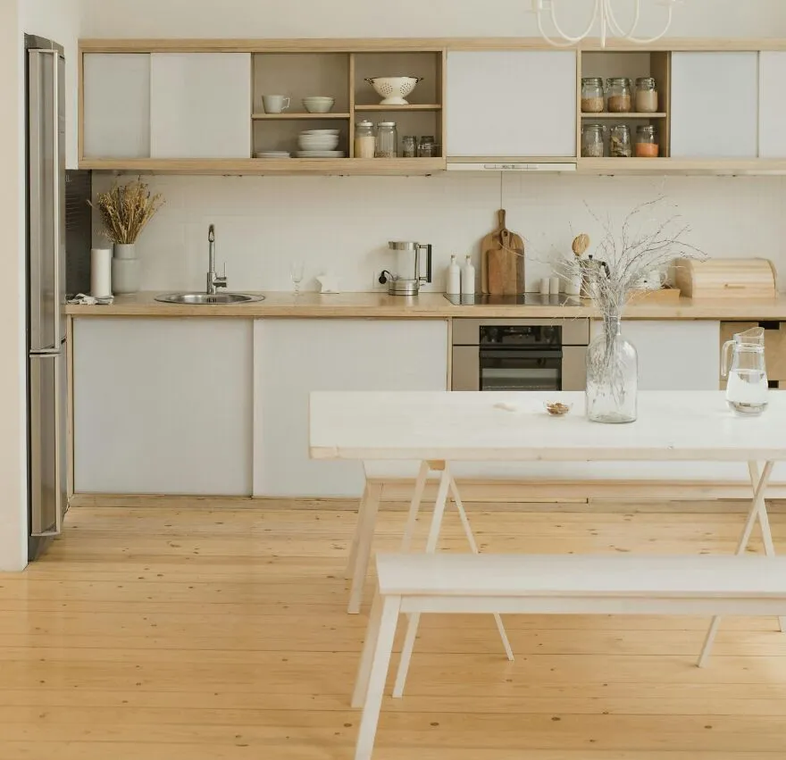 Dining table with a vase in front of modern and stylish kitchen cabinets in wooden and white colors.
