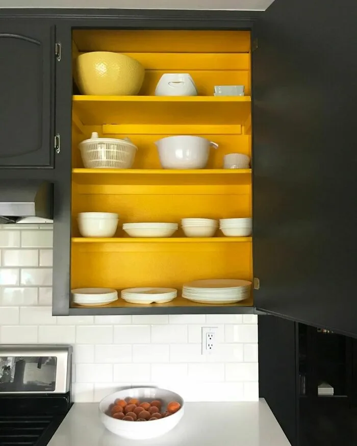 Black kitchen cabinet with bright yellow painted shelves, showcasing white dishes for a modern and stylish kitchen cabinets design.