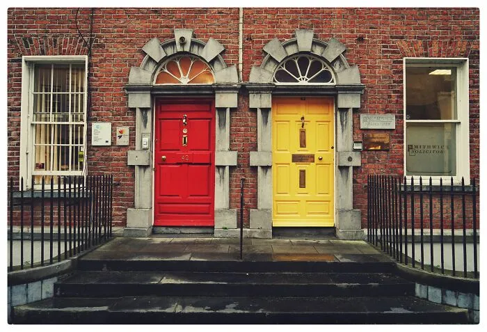 Two colorful wooden doors, one red and one yellow, on a brick building, symbolizing choices and riddles.