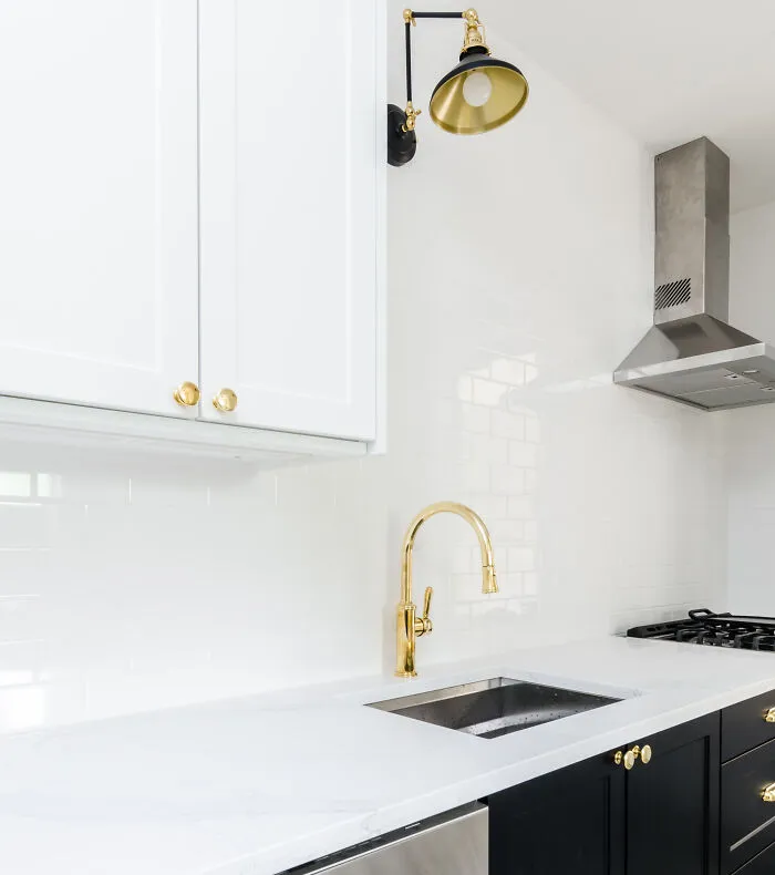 White and black modern kitchen cabinets with gold hardware, a sleek faucet, and a stainless steel range hood in a stylish kitchen design
