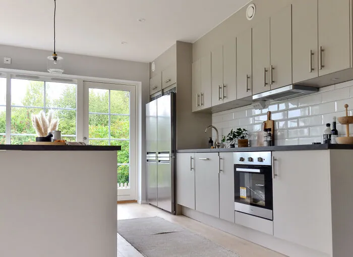 Light gray kitchen with modern and stylish kitchen cabinets and a large steel refrigerator near a bright window.