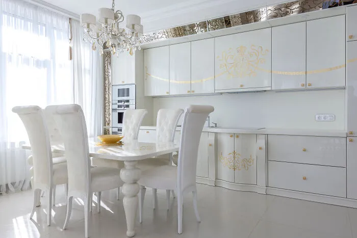 Bright white kitchen featuring modern and stylish kitchen cabinets with gold accents and a large dining table with chairs.