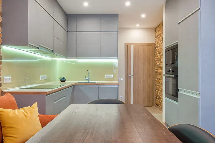 Gray kitchen cabinets with under-cabinet lighting and a wooden table with colorful cushions in a modern kitchen setting