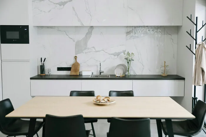 Modern and stylish kitchen cabinets with a black countertop and marble backsplash in a bright dining area.