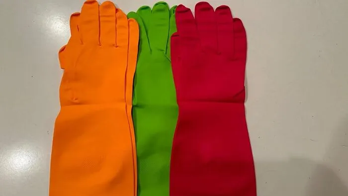 Three colorful cleaning gloves—orange, green, and red—laid out for a pre-2025 cleaning mission.