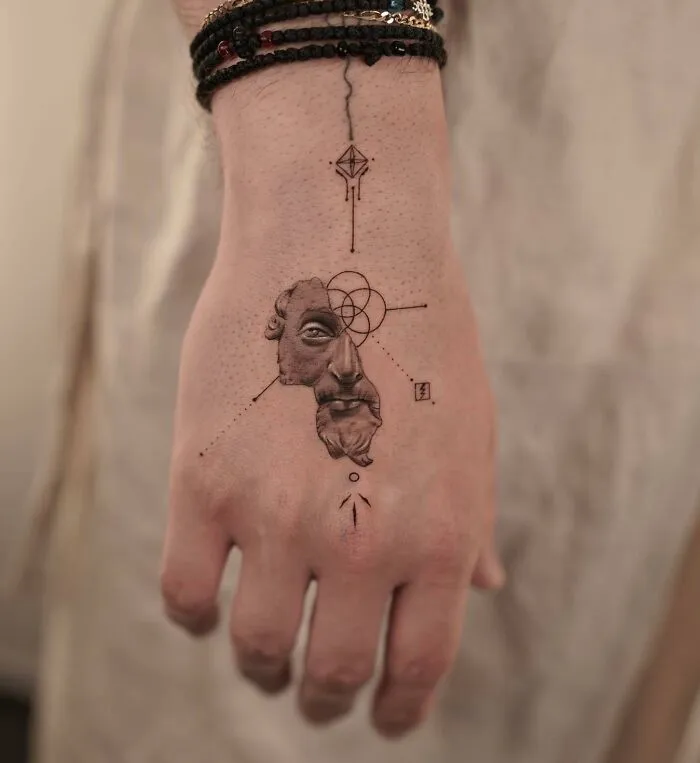 Abstract small hand tattoo with geometric shapes and a classical face design.