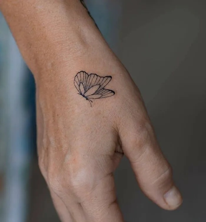 Small hand tattoo featuring a delicate butterfly design on the back of the hand.