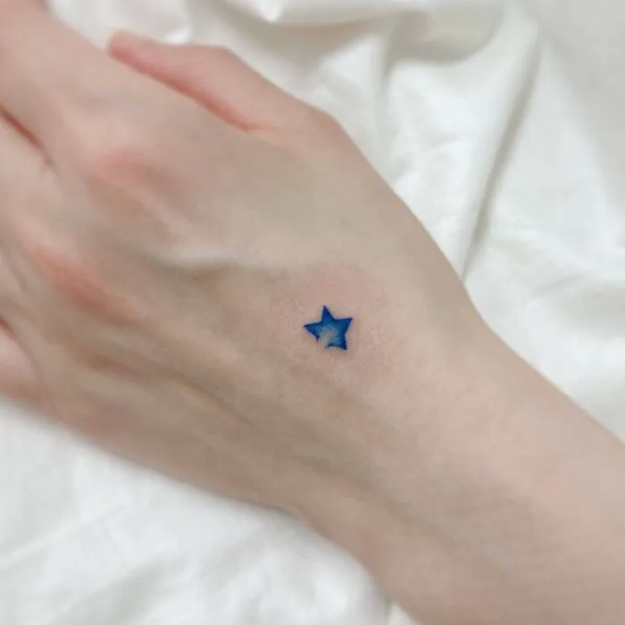 Small hand tattoo featuring a blue star on the back of a hand.